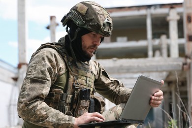 Military mission. Soldier in uniform using laptop near abandoned building outside