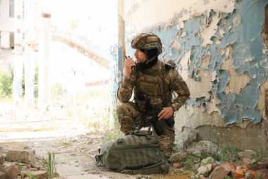 Military mission. Soldier in uniform radio transmitter near abandoned building outdoors