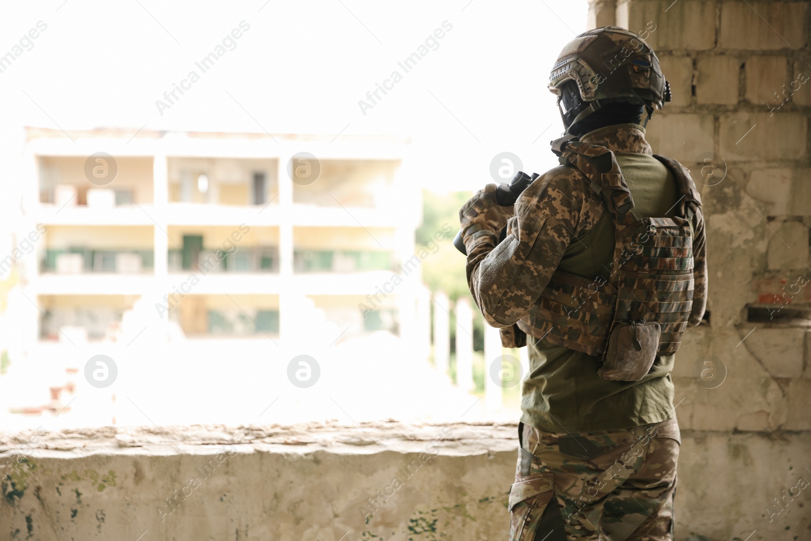 Photo of Military mission. Soldier in uniform with binoculars inside abandoned building, back view. Space for text