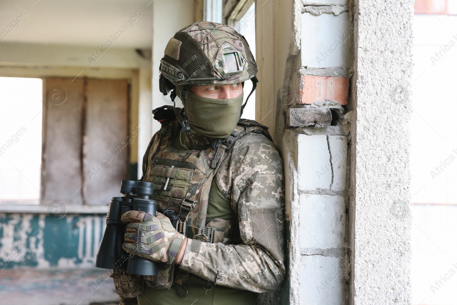Photo of Military mission. Soldier in uniform with binoculars inside abandoned building
