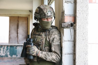 Military mission. Soldier in uniform with binoculars inside abandoned building