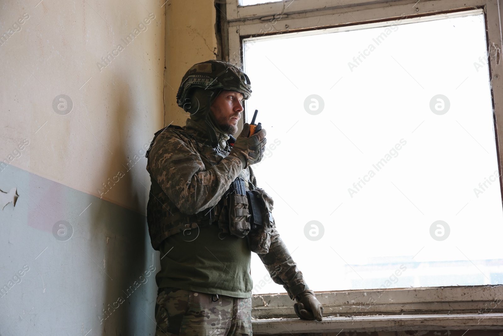 Photo of Military mission. Soldier in uniform with radio transmitter inside abandoned building, space for text