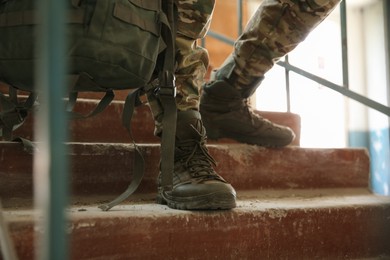 Military mission. Soldier in uniform on stairs inside abandoned building, closeup