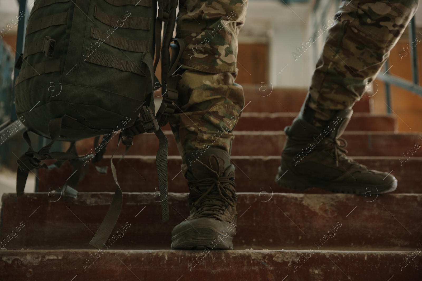 Photo of Military mission. Soldier in uniform on stairs inside abandoned building, closeup