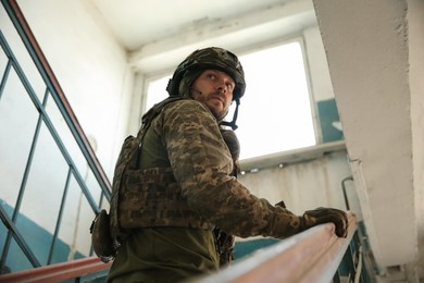 Military mission. Soldier in uniform on stairs inside abandoned building, low angle view