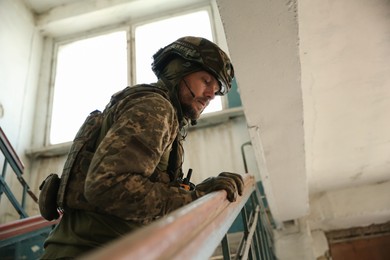 Military mission. Soldier in uniform on stairs inside abandoned building, low angle view. Space for text