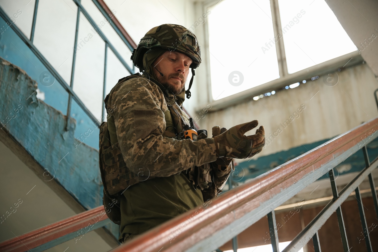 Photo of Military mission. Soldier in uniform on stairs inside abandoned building, low angle view