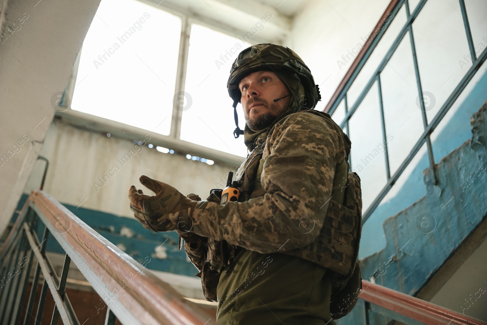 Photo of Military mission. Soldier in uniform on stairs inside abandoned building, low angle view