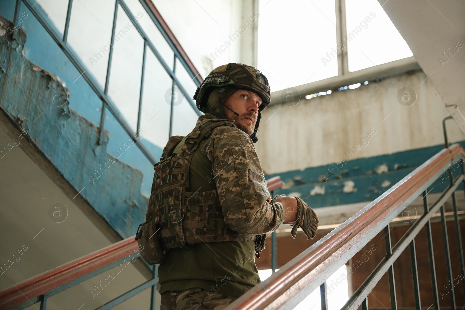 Photo of Military mission. Soldier in uniform on stairs inside abandoned building, low angle view
