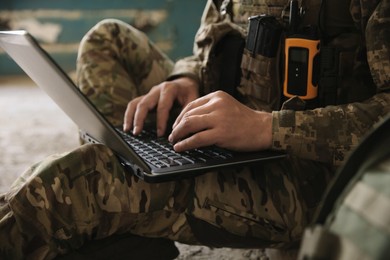 Military mission. Soldier in uniform using laptop inside abandoned building, closeup