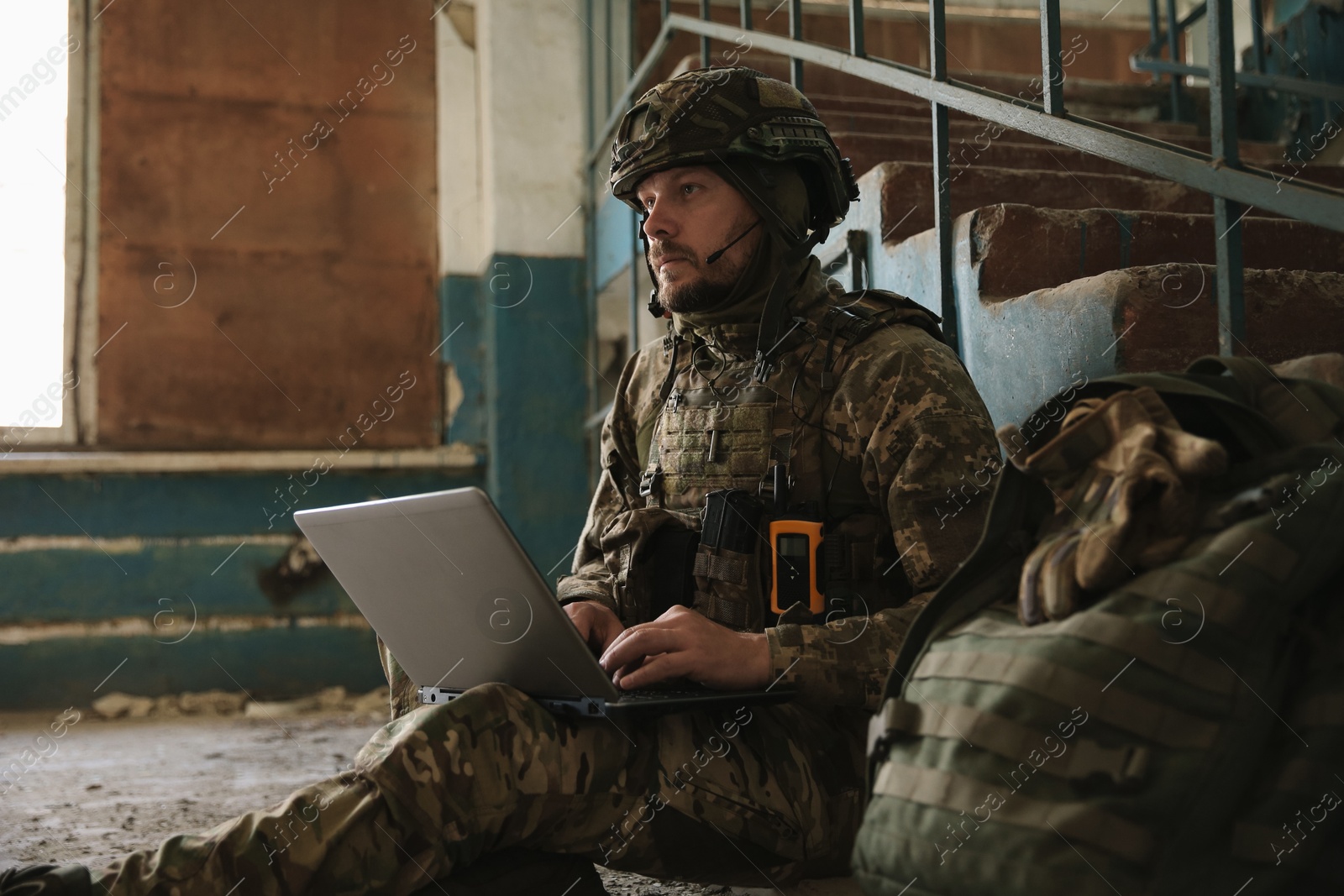 Photo of Military mission. Soldier in uniform using laptop inside abandoned building