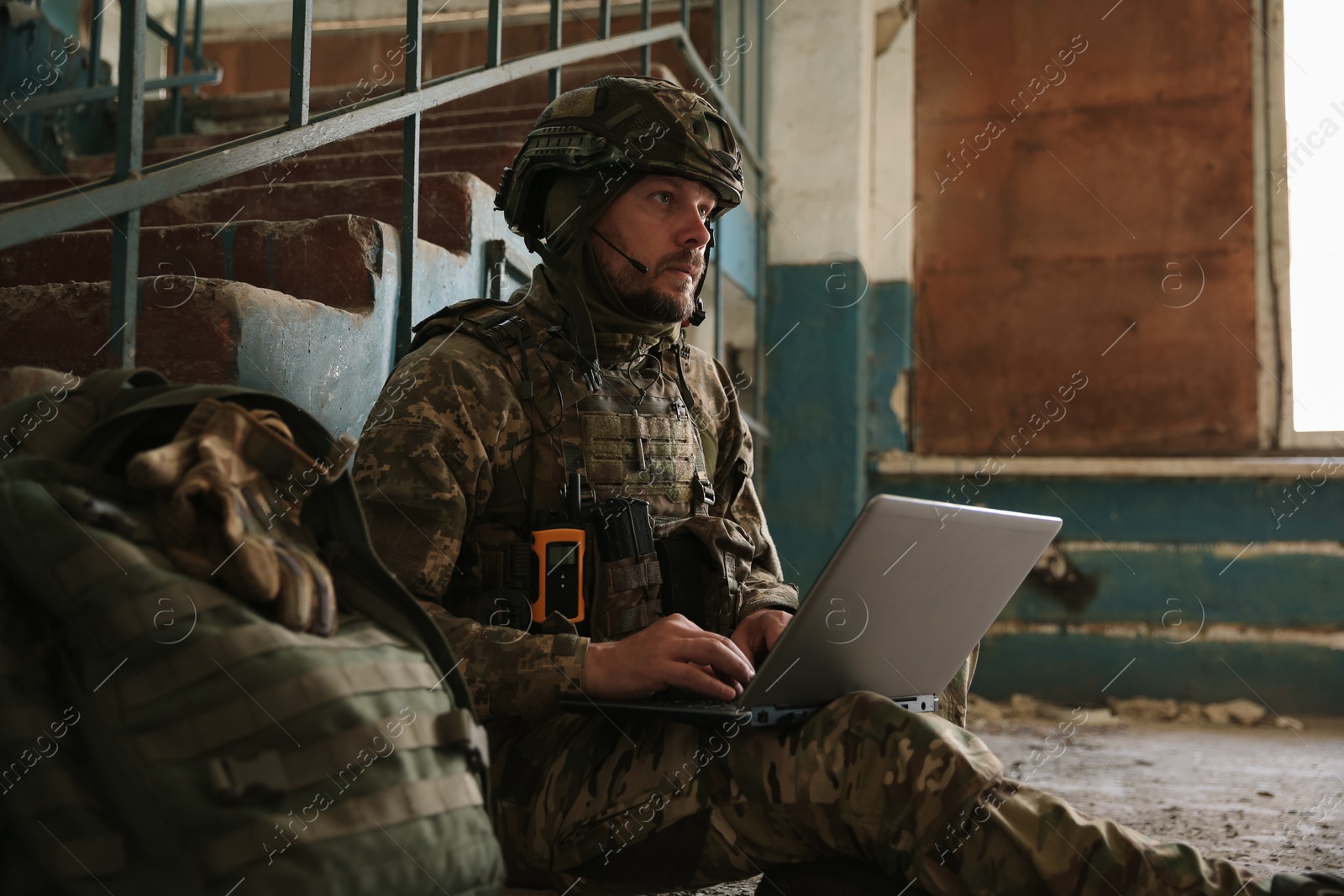 Photo of Military mission. Soldier in uniform using laptop inside abandoned building