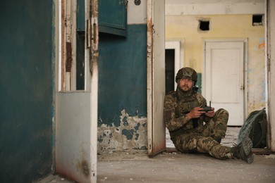 Photo of Military mission. Soldier in uniform with drone controller inside abandoned building