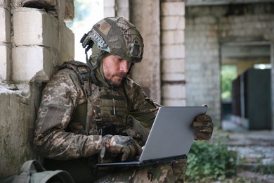 Military mission. Soldier in uniform using laptop inside abandoned building