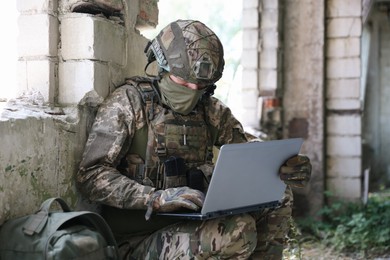 Photo of Military mission. Soldier in uniform using laptop inside abandoned building
