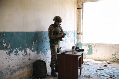 Photo of Military mission. Soldier in uniform at table inside abandoned building