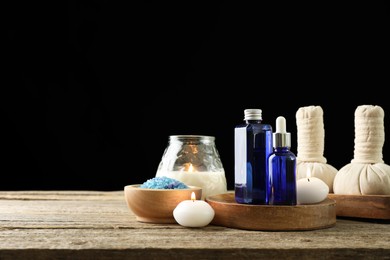 Photo of Spa composition. Cosmetic products, herbal bags, burning candles and sea salt on wooden table against black background, space for text