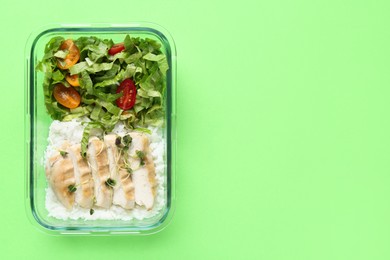 Healthy meal. Fresh salad, rice and chicken in glass container on green background, top view. Space for text