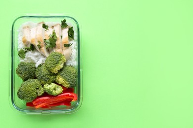 Photo of Healthy meal. Fresh broccoli, pepper, chicken and rice in glass container on green background, top view. Space for text