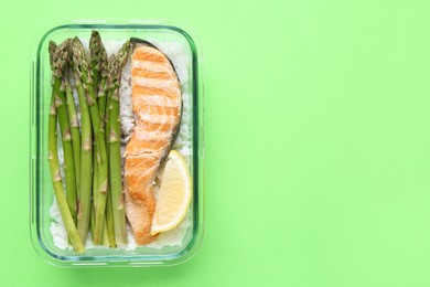 Photo of Healthy meal. Fresh asparagus, salmon, rice and lemon in glass container on green background, top view. Space for text