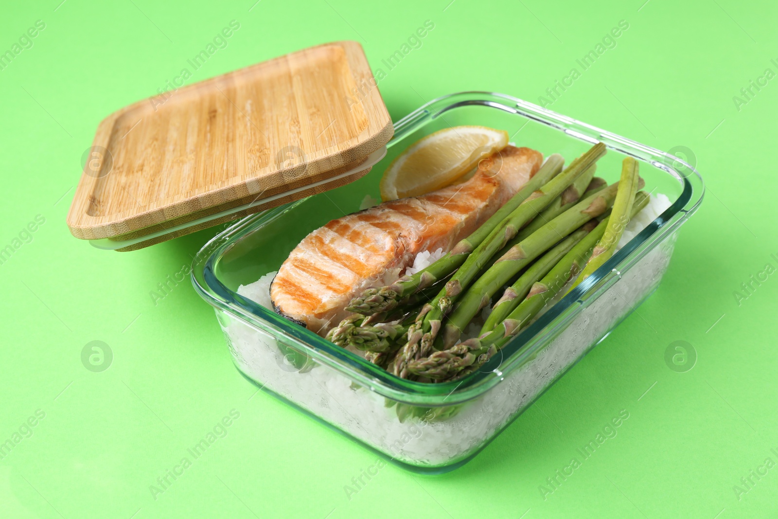 Photo of Healthy meal. Fresh asparagus, salmon and rice in glass container on green background