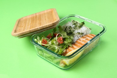 Photo of Healthy meal. Fresh salad, salmon and rice in glass container on green background