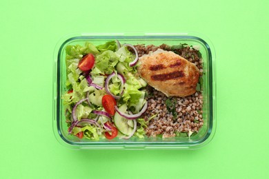 Photo of Healthy meal. Fresh salad, cutlet and buckwheat in glass container on green background, top view