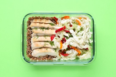 Photo of Healthy meal. Fresh salad, chicken and buckwheat in glass container on green background, top view