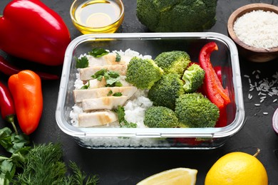 Photo of Healthy meal. Fresh broccoli, chicken, rice and pepper in glass container near other products on black table