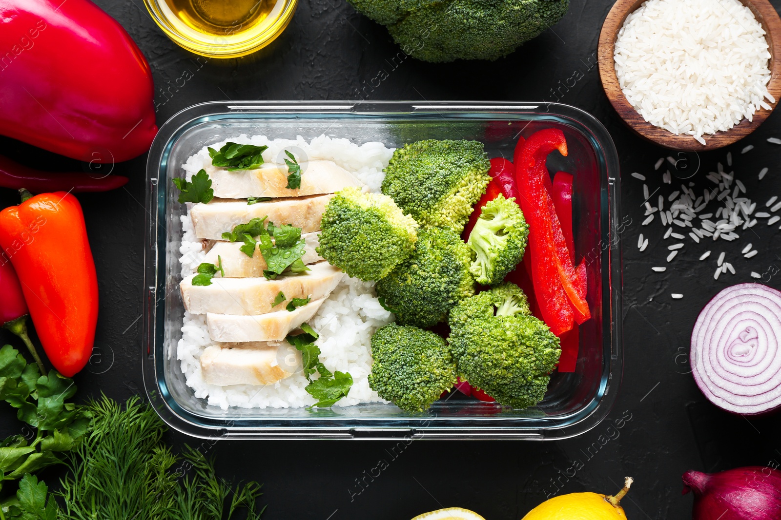 Photo of Healthy meal. Fresh broccoli, chicken, rice and pepper in glass container near other products on black table, flat lay