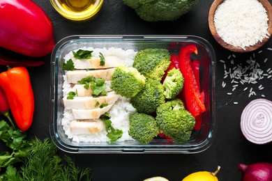 Photo of Healthy meal. Fresh broccoli, chicken, rice and pepper in glass container near other products on black table, flat lay