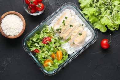 Photo of Healthy meal. Fresh salad, chicken and rice in glass container near other products on black table, flat lay