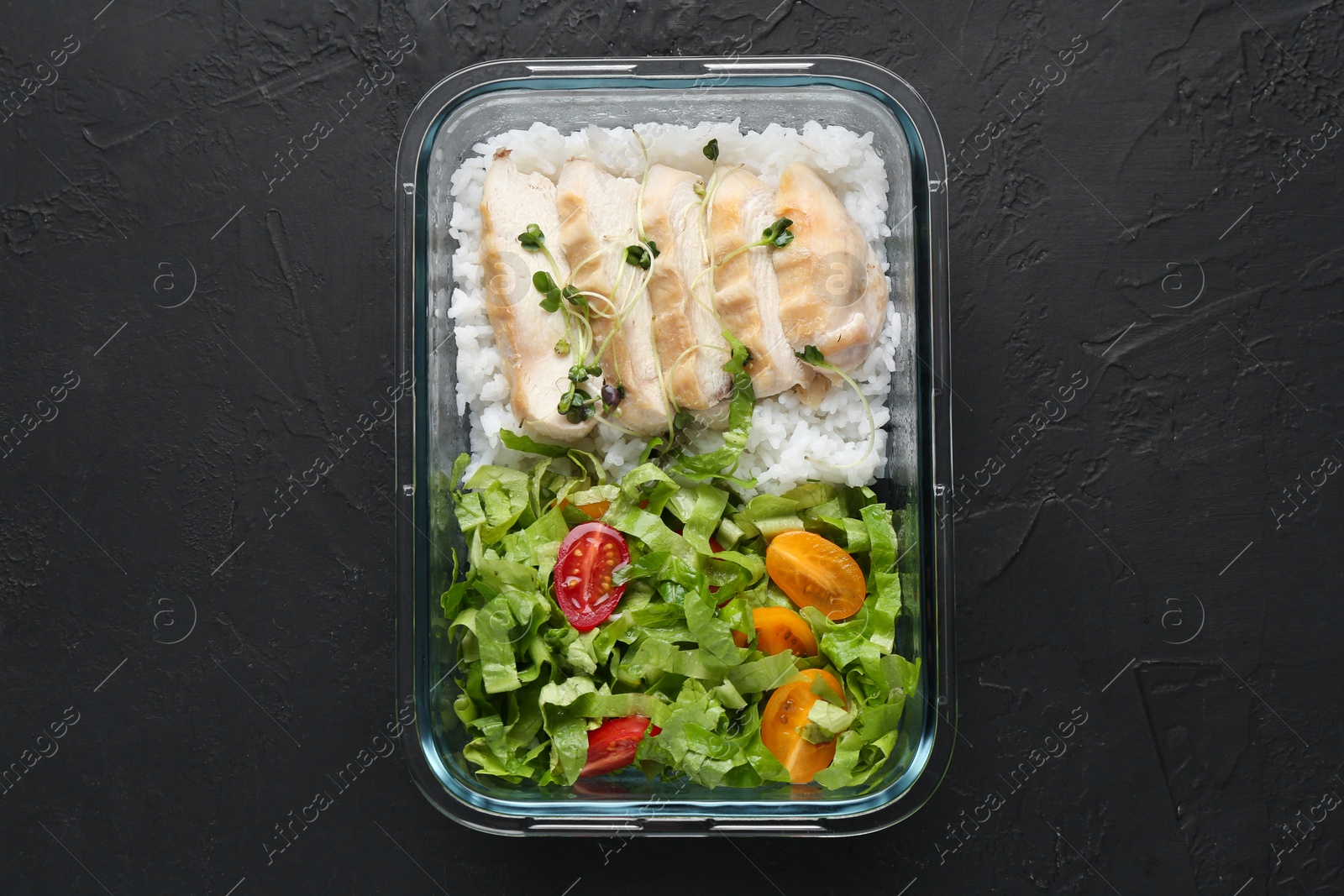 Photo of Healthy meal. Fresh salad, chicken and rice in glass container on black table, top view