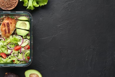 Photo of Healthy meal. Fresh salad, avocado, cutlet and buckwheat in glass container near other products on black table, flat lay. Space for text