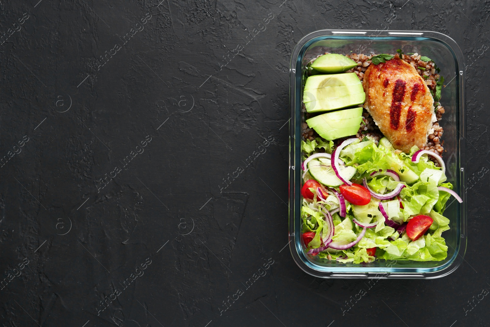 Photo of Healthy meal. Fresh salad, avocado, cutlet and buckwheat in glass container on black table, top view. Space for text
