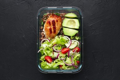 Photo of Healthy meal. Fresh salad, avocado, cutlet and buckwheat in glass container on black table, top view