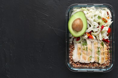 Photo of Healthy meal. Fresh salad, avocado, chicken and buckwheat in glass container on black table, top view. Space for text