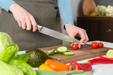 Photo of Healthy food. Woman cutting tomato at white table in kitchen, closeup