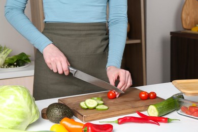 Healthy food. Woman cutting tomato at white table in kitchen, closeup