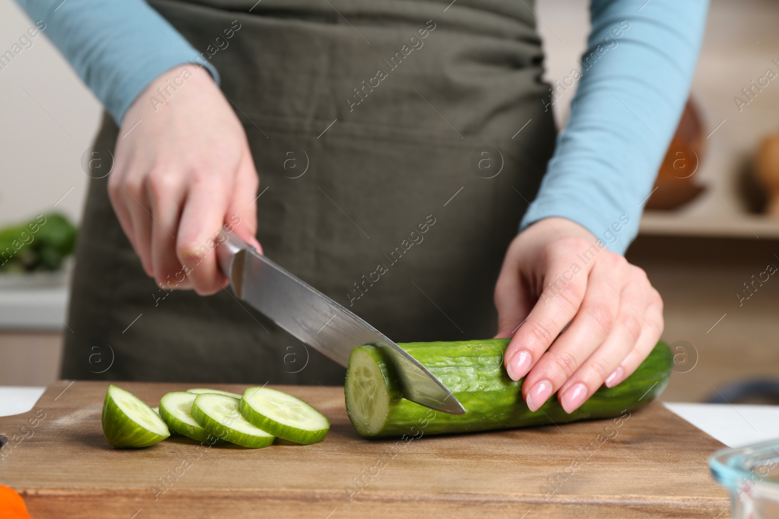 Photo of Healthy food. Woman cutting cucumber at table in kitchen, closeup