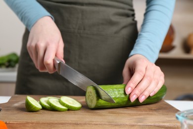 Healthy food. Woman cutting cucumber at table in kitchen, closeup