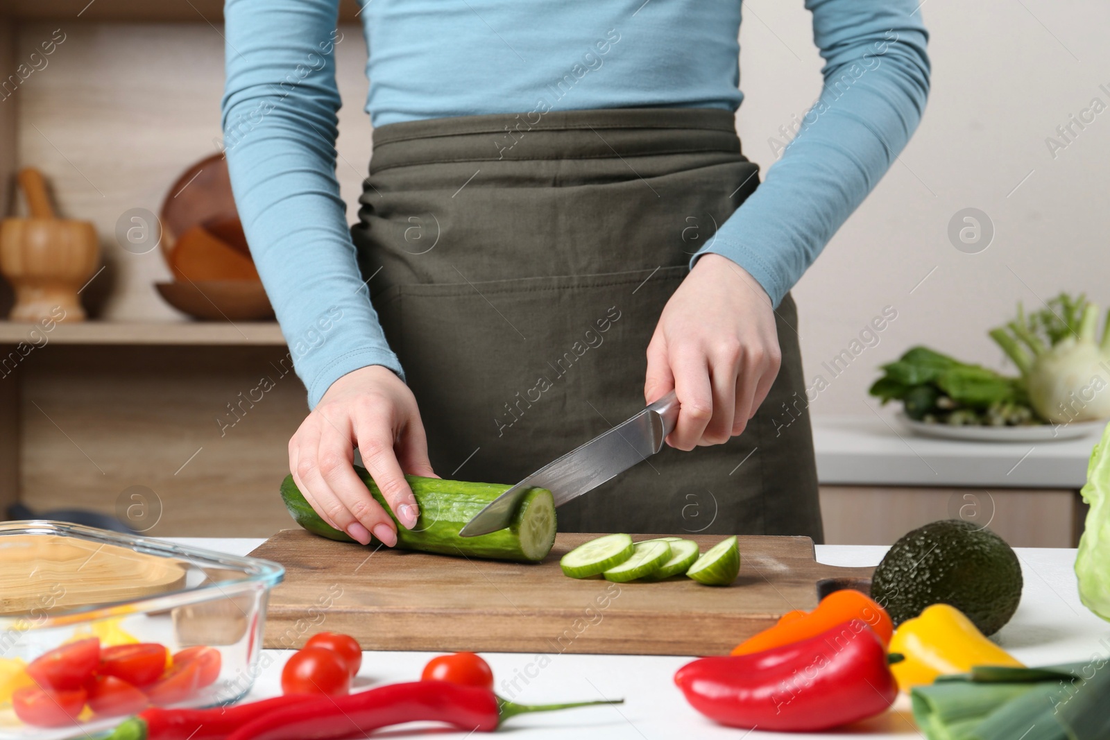 Photo of Healthy food. Woman cutting cucumber at white table in kitchen, closeup