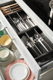 Photo of Ceramic dishware and cutlery in drawers indoors