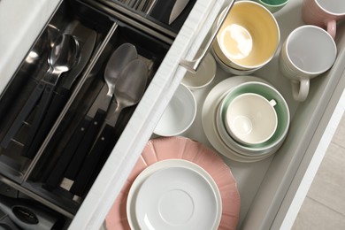 Ceramic dishware and cutlery in drawers indoors, top view