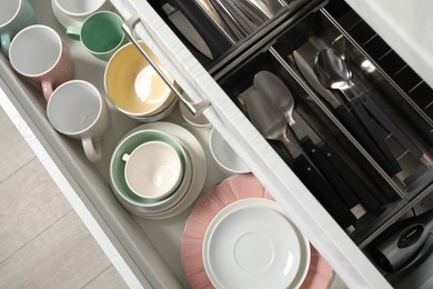 Photo of Ceramic dishware and cutlery in drawers indoors, above view