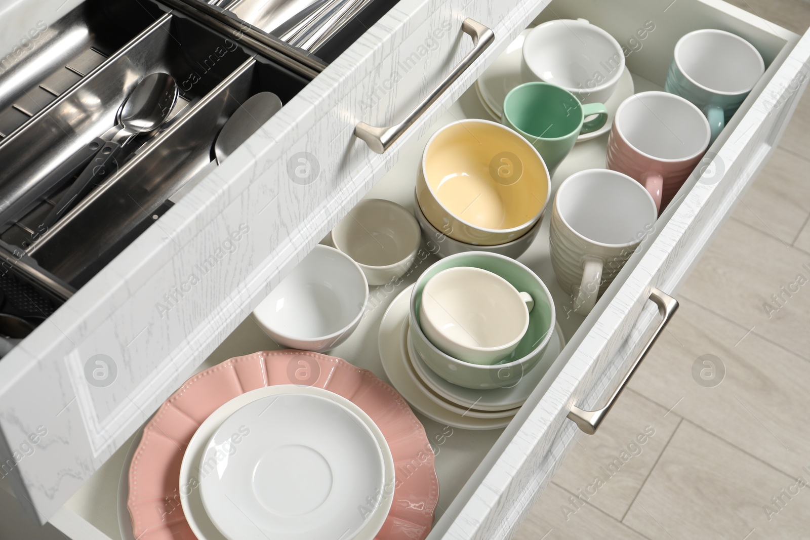 Photo of Ceramic dishware and cutlery in drawers indoors