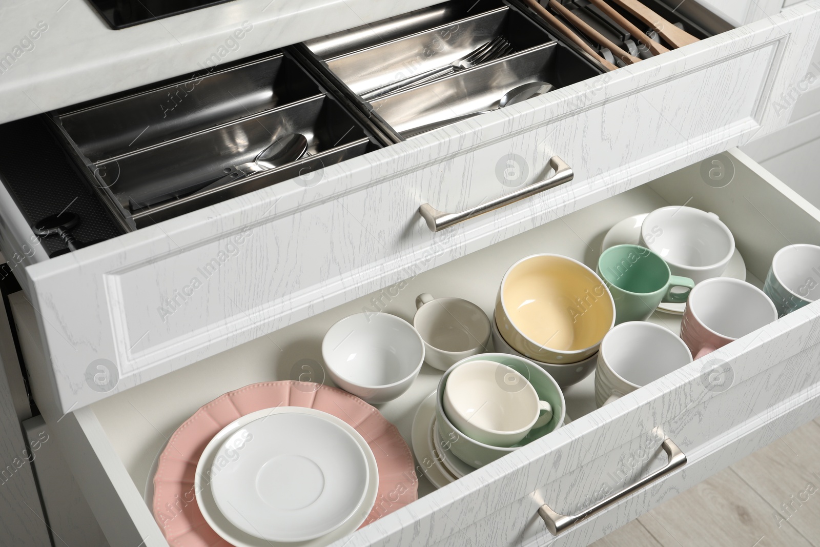 Photo of Ceramic dishware and cutlery in drawers indoors