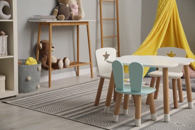 Photo of Stylish child room interior with table, chairs, toys and play tent