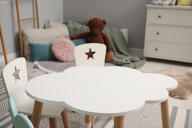 Photo of Stylish child room interior with table, chairs, toy bear and chest of drawers