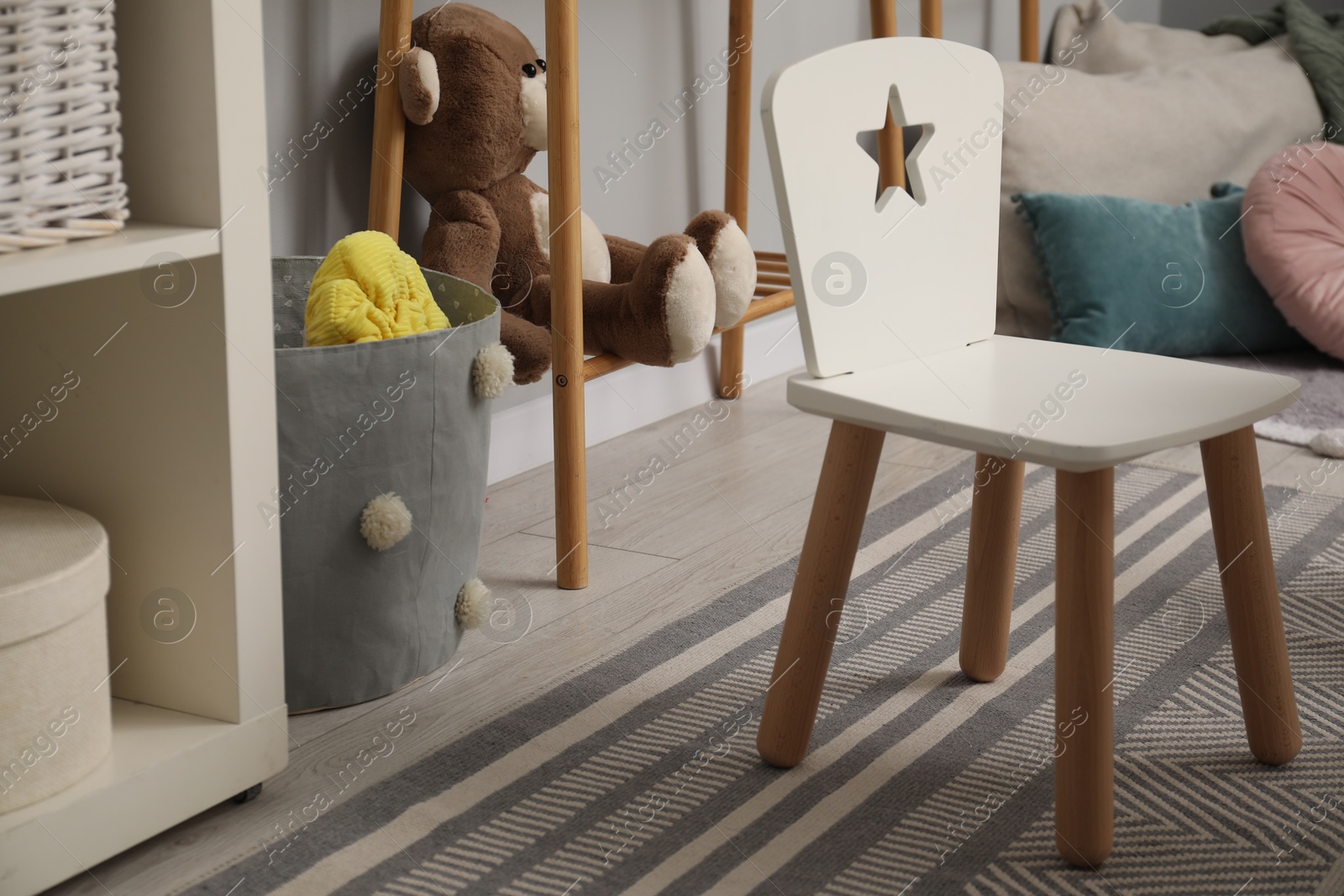 Photo of Small chair, teddy bear and pillows in child room. Interior design